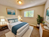 A fully decorated bedroom with blue accented decor, two table lamps, large potted plant, white rug and a made up bed.