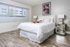 A neatly made white bed with white bedsheets sits on grey vinyl flooring, complemented by a window and decorative wall art in the background
