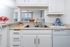 A stainless steel kitchen sink is integrated into white cabinets, complemented by nickel-finished hardware, creating a sleek and modern look