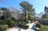 Apartment complex with modern buildings, landscaped gardens, and a central pathway lined with trees and shrubs under a clear blue sky.