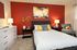 A cozy bedroom featuring a striking red accent wall and a neatly made bed, creating a warm and inviting atmosphere.