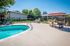 Outdoor pool area with lounge chairs and umbrellas surrounded by a fence and trees, set in a residential community under a clear blue sky.