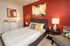 A cozy bedroom featuring a striking red accent wall and a neatly made bed, creating a warm and inviting atmosphere.