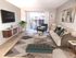 Modern living room with a large TV, abstract paintings, green armchair, beige sofa, and geometric rug. A wooden cabinet and green bench complement the decor. Glass doors reveal a patio view.