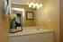 well lit bathroom including a large vanity with lots of storage, toilet and towel bar