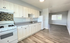 A bright kitchen with white cabinets and appliances, including a stove and fridge. It features a mosaic tile backsplash and gray countertops, opening to a wood-floored living area.