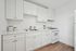 A bright kitchen with white cabinets, a sleek stainless steel sink, and a compact gas stove. Minimalist decor on the countertop and wood flooring.