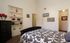 A cozy bedroom with a patterned bedspread, black dresser, and built-in shelves. Decor includes red accents, framed art, and soft lighting, creating a warm atmosphere.