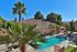 Emerald Pointe Apartment complex, with a sunny courtyard, features a blue swimming pool, surrounded by palm trees, beige buildings with red-tiled roofs, and clear skies.