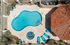 Aerial view of a small, bean-shaped swimming pool surrounded by a patio. Features include turquoise lounge chairs, round tables with umbrellas, and a red tiled roof corner. The setting is bright and inviting, evoking relaxation.