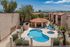 A serene courtyard features a kidney-shaped pool, surrounded by beige buildings with terracotta roofs. Blue lounge chairs and a small hot tub add a relaxing vibe.