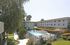 Outdoor apartment courtyard with a pool surrounded by lounge chairs and umbrellas, flanked by two apartment buildings. The setting is sunny and tranquil.