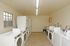 Laundry room with tiled floors, fluorescent lighting, and washers and dryers along both walls. A small window and bulletin board are visible.