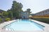 Apartment complex with a clear pool, colorful inflatables, and lounge chairs. Surrounded by hedges and trees under a sunny sky. Relaxing ambiance.