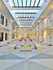 Bright atrium with geometric flooring, skylight ceiling, and two levels of white balcony rooms. Orange chairs add a pop of color, creating a modern atmosphere.