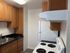 Kitchen with wooden cabinets, black countertop, white refrigerator, electric stove, sink, and vent hood under bright ceiling light.