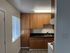 Small kitchen with wooden cabinets, black countertop, stainless steel sink, white stove, and a window with blinds letting in natural light.