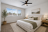 White walls, brown carpet, brown ceiling fan with wide window on left back wall
