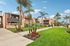 Charming apartment complex with lush green lawns, vibrant flower beds, and beautiful palm trees under a clear blue sky.