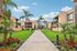 Charming apartment complex with lush green lawns, vibrant flower beds, and towering palm trees under a bright blue sky.