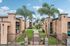 Charming apartment complex featuring lush landscaping, tall palm trees, and a welcoming gated entrance under a clear blue sky.