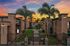 Exquisite apartment complex entrance flanked by palm trees, with a vibrant sunset sky creating a serene and inviting atmosphere.
