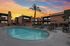 Charming apartment complex with a pristine swimming pool, inviting outdoor seating, and a vibrant sunset backdrop.