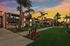 Charming apartment complex surrounded by lush green lawns and vibrant flower beds, highlighted by a stunning sunset sky.