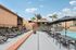 Charming outdoor pool area with sun loungers and shaded seating, surrounded by lush palm trees and vibrant summer sky.