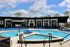 Modern apartment complex with elegant swimming pool and ample sun loungers under a bright blue sky.