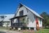 Quaint white cottage with a metal roof, featuring a cozy front porch and lush landscaping.