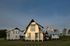 Stunning modern farmhouse on vast green landscape with blue sky backdrop.