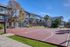 Bright and inviting apartment exterior with a lush backdrop, featuring a well-maintained basketball court for active community living.