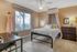 Elegant bedroom with soft peach walls, featuring a cozy bed with a sheer canopy, large window with natural light, stylish dresser, and a functional desk, creating a serene and inviting atmosphere.