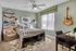 Cozy bedroom with stylish decor, featuring a plush armchair, wall-mounted guitar, and large window letting in natural light.