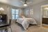 Cozy bedroom with soft carpet, a stylish bed with plush pillows, and elegant framed artwork. Natural light fills the room through wide windows, creating an inviting and vibrant ambiance.