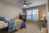 Inviting bedroom with cozy blue bedding, sleek ceiling fan, and abundant natural light through large windows, ideal for relaxation.