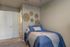 Cozy bedroom with stylish blue bedding, elegant wall decor, and plush carpeting, creating a serene atmosphere.