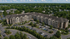 Elegant four-story apartment complex nestled in lush greenery with ample parking and modern architecture.