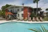 Photo of community swimming pool area with outdoor seating and umbrellas, with apartment building in background.