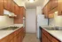Photo showing galley style kitchen, with vinyl tile flooring, wood-style cabinets, electric stove with hood, counter-height oven, refrigerator, dishwasher, and double sided sink with spray nozzle.