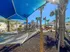 Outdoor relaxation area with hammocks and palm trees under blue canopies in a sunny apartment complex.