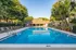 Inviting outdoor pool area surrounded by lush greenery and sun loungers, adjacent to a cozy clubhouse.