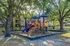Charming playground with colorful slides and structures under a canopy of lush trees.
