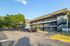 Three-story apartment building with balconies, surrounded by trees and ample parking.