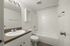 Modern white bathroom featuring a stylish vanity, spacious mirror, and a pristine bathtub with tile accents.