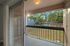 Charming balcony with sliding glass doors overlooking a serene outdoor area with trees and a sunlit sky.