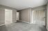 Bright, empty room with plush carpet, white doors, and vertical blinds leading to a balcony.