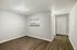 Bright entryway with wooden floors, a view into the modern kitchen through a cutout, and a white door.