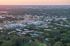 Aerial view of a vibrant apartment community surrounded by lush greenery and cityscape at sunset.